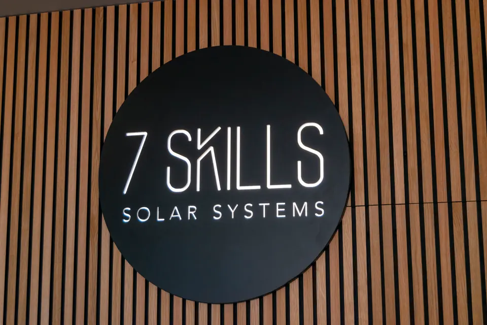Logótipo circular da 7 Skills Solar Systems, iluminado, numa parede de ripado de madeira, na loja.